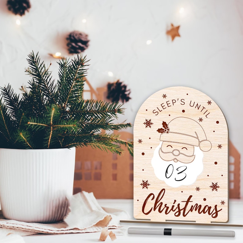 May include: A wooden countdown sign with a Santa Claus illustration and the text "Sleep's Until Christmas". The sign has a white background with brown text and snowflakes. The number "03" is written on the sign.