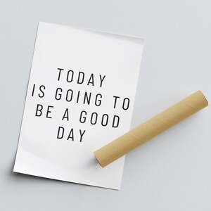 K&ouml;nnte beinhalten: Ein wei&szlig;es Poster mit dem Text "TODAY IS GOING TO BE A GOOD DAY" in schwarzer Schrift. Daneben liegt eine braune Papprolle auf einer hellgrauen Oberfl&auml;che.