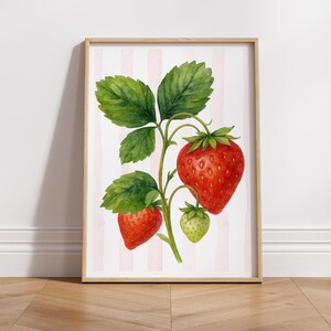 May include: A framed watercolor print of a strawberry plant. The image features three ripe red strawberries and one unripe green strawberry, with green leaves and stems. The background has pink and white vertical stripes.
