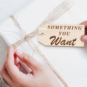 K&ouml;nnte beinhalten: Eine wei&szlig;e Geschenkbox, die mit Schnur umwickelt ist und ein Holzschild mit der Aufschrift "Something You Want".
