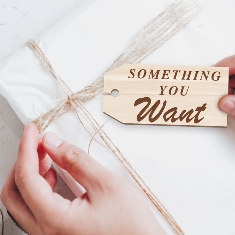 K&ouml;nnte beinhalten: Eine wei&szlig;e Geschenkbox, die mit Schnur umwickelt ist und ein Holzschild mit der Aufschrift "Something You Want".