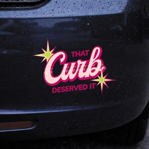 May include: A bumper sticker with the text "That Curb Deserved It" in pink and white script. The sticker has a black background with green starburst accents.