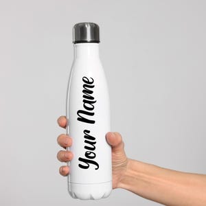May include: A white insulated water bottle with a silver cap, held by a hand. The bottle has the words "Your Name" in a black script font. The bottle is designed to keep drinks cold or hot.