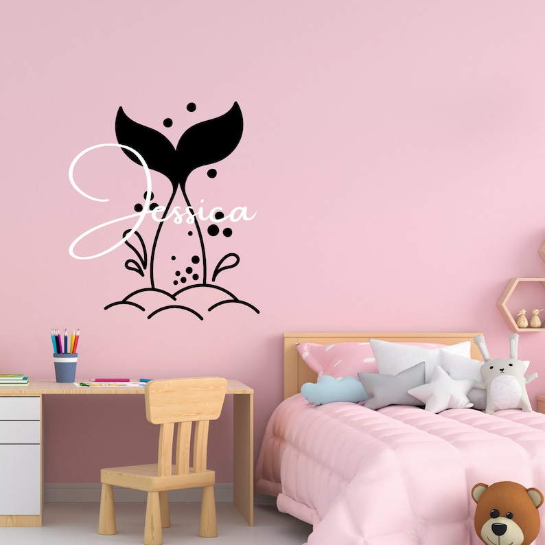 May include: Black and white mermaid tail wall decal with the name Jessica. The decal is on a pink wall in a child's bedroom.