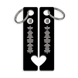 May include: Black metal keychain with a heart-shaped cutout. The keychain features a white sound wave design and a silver ring.