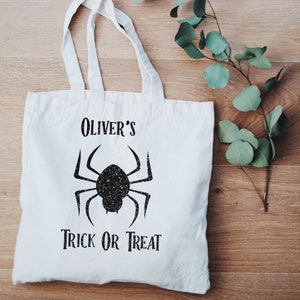K&ouml;nnte beinhalten: Wei&szlig;e Stofftasche mit schwarzem Text und einer schwarzen Spinnengrafik. Der Text lautet "Oliver's Trick or Treat".