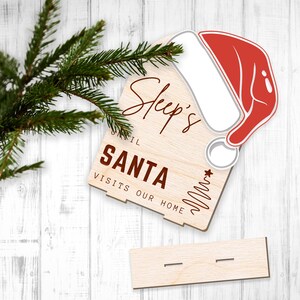 May include: Wooden sign with the text "Sleep's until Santa visits our home" and a red and white Santa hat.