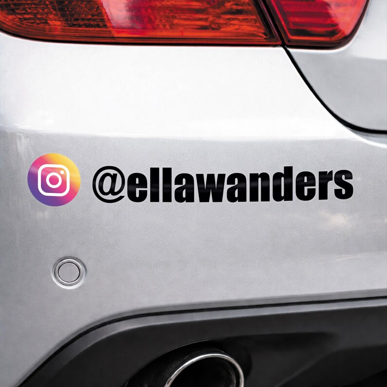 May include: A white car bumper with a black sticker featuring the Instagram logo and the username @ellawanders. The Instagram logo is a gradient of orange, yellow, pink, and purple.