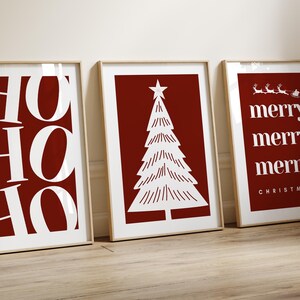 May include: Three framed Christmas art prints. The prints feature white text and illustrations on a red background. One print says "HO HO HO", another has a Christmas tree, and the third says "merry" multiple times with a Santa sleigh.