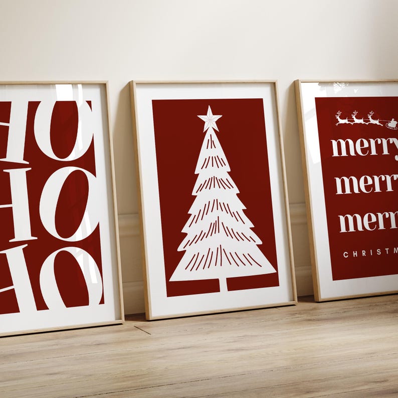 May include: Three framed Christmas art prints. The prints feature white text and illustrations on a red background. One print says "HO HO HO", another has a Christmas tree, and the third says "merry" multiple times with a Santa sleigh.
