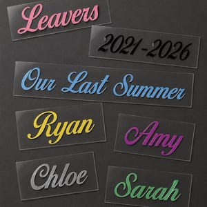 May include: A collection of clear acrylic name tags and labels with various text in different colors. The labels include the words "Leavers," "Our Last Summer," and names like "Ryan," "Amy," "Chloe," and "Sarah." The year range "2021-2026" is also displayed.