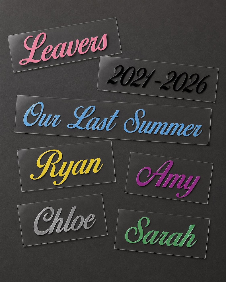 May include: A collection of clear acrylic name tags and labels with various text in different colors. The labels include the words "Leavers," "Our Last Summer," and names like "Ryan," "Amy," "Chloe," and "Sarah." The year range "2021-2026" is also displayed.