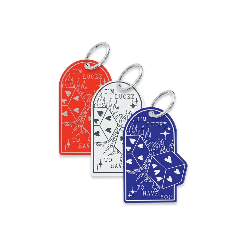Puede incluir: Tres llaveros con un dise&ntilde;o de dados y llamas. Los llaveros son rojo, blanco y azul. El texto en los llaveros dice "I'm Lucky to Have You".