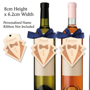 May include: Two wine bottles with personalized wooden tags. The tags are shaped like a tuxedo and have the names "Groom" and "Frank" printed on them. The tags are 8 cm high and 6.2 cm wide.