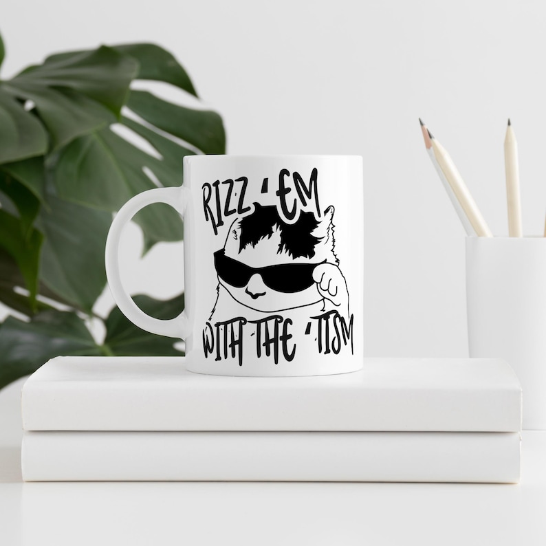 May include: White ceramic mug featuring a black and white illustration of a cat wearing sunglasses and the text "Rizz 'em with the -tism".