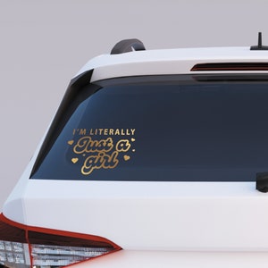 K&ouml;nnte beinhalten: Goldener Vinyl-Aufkleber mit dem Text "I'm literally just a girl" mit Herzen um den Text. Der Aufkleber befindet sich auf der Heckscheibe eines wei&szlig;en Autos.