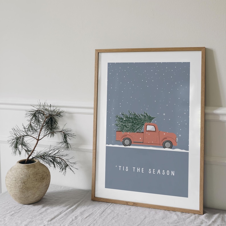 May include: A framed print of a red pickup truck carrying a Christmas tree against a blue snowy background. The text 'Tis the Season is printed below the truck.