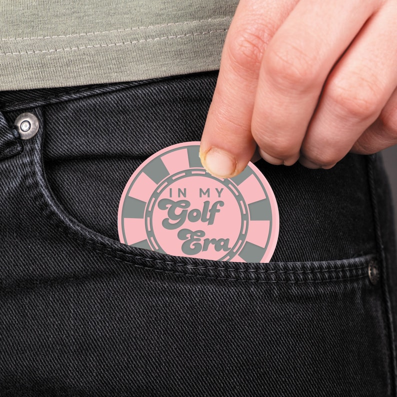 May include: A pink and gray round sticker with the text "In My Golf Era" in a retro font.