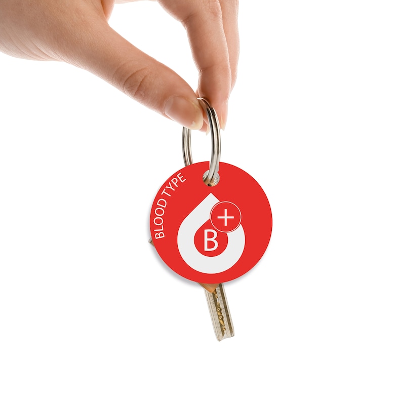 May include: A red round keychain with the text "BLOOD TYPE" and a white blood drop with a "B+" inside. The keychain is attached to a silver key ring.