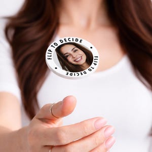May include: A white circular coin with the text "Flip to Decide" around the edge and a smiling woman's face in the center. The coin is being flipped in the air.