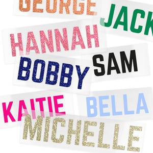 May include: A collection of name decals in various colors and fonts. Names include "George", "Jack", "Hannah", "Bobby", "Sam", "Kaitie", "Bella", and "Michelle". The names are printed on clear rectangular stickers.