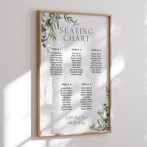 May include: A framed seating chart with a wooden frame. The chart features names organized under table numbers, with decorative green foliage. The text at the top reads "the SEATING CHART" and at the bottom "Celebrating Joy's 40th Birthday".