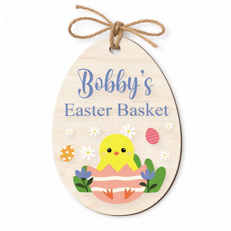 May include: Wooden Easter egg-shaped sign with the text "Bobby's Easter Basket" in blue script. The sign features a yellow chick hatching from a pink and white striped egg, surrounded by flowers and Easter eggs, and is topped with a twine bow.