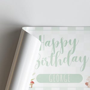 May include: A birthday-themed print with the words "Happy Birthday George" in a soft green script. The background has a subtle checkered pattern in light green. A corner of the print is folded over, revealing a white edge.