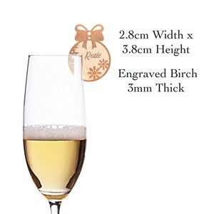 May include: A wooden Christmas ornament with a bow and snowflake design. The ornament is engraved with the name "Rosie" and measures 2.8 inches wide by 3.8 inches tall. It is made of 3mm thick birch wood.