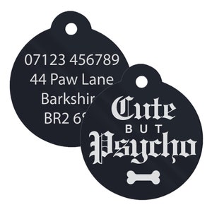 May include: Black round dog tag with white text. The tag has a phone number, address, and the text "Cute But Psycho" with a bone symbol.