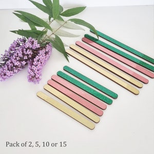May include: A set of 15 wooden craft sticks with glitter. The sticks are in three colors: green, pink, and gold. Pack of 2, 5, 10 or 15.