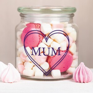 May include: A glass jar filled with pink and white marshmallows and macarons. The jar has a heart-shaped design with the word "MUM" inside.