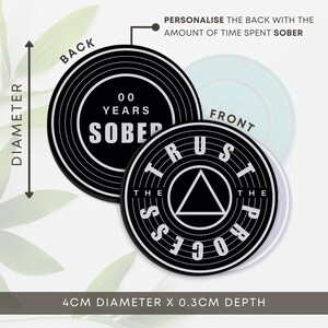 May include: Black and white coaster with the words "Trust the Process" and a triangle in the centre. The back of the coaster is black with white concentric circles and the text "00 Years Sober". The coaster is 4 cm in diameter and 0.3 cm deep.