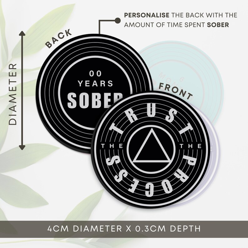 May include: Black and white coaster with the words "Trust the Process" and a triangle in the centre. The back of the coaster is black with white concentric circles and the text "00 Years Sober". The coaster is 4 cm in diameter and 0.3 cm deep.