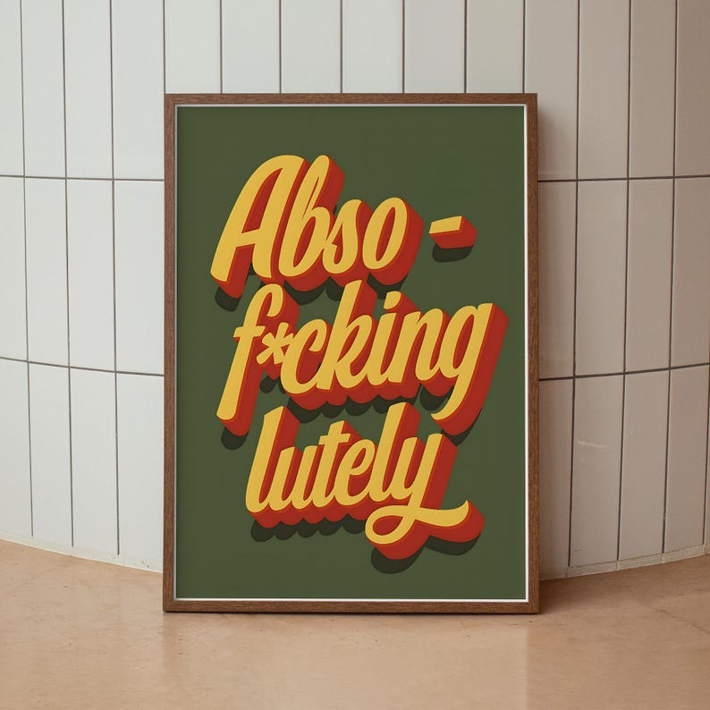 Puede incluir: Un p&oacute;ster enmarcado con la frase "Abso-f*cking-lutely" en letras 3D amarillas y rojas sobre un fondo verde oscuro. La impresi&oacute;n est&aacute; enmarcada en un marco de madera marr&oacute;n.