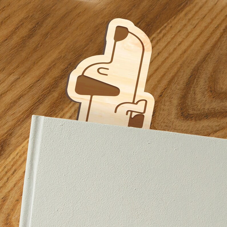 May include: Wooden bookmark shaped like a dog with a brown outline. The bookmark is standing upright on a white book.
