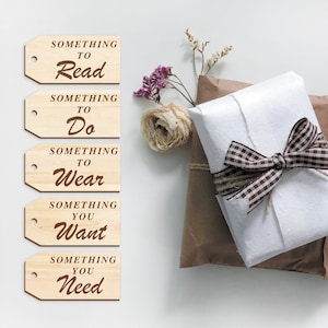 K&ouml;nnte beinhalten: F&uuml;nf Holz-Geschenk-Etiketten mit braunem Text. Die Etiketten lauten "Something to Read", "Something to Do", "Something to Wear", "Something You Want" und "Something You Need".