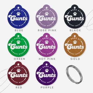 Op de afbeelding: Negen verschillende gekleurde hondenpenningen met de tekst "I bark at Cunts" en "Woof Woof" in witte letters. De kleuren zijn blauw, roze, zwart, groen, roze, goud, rood, paars en zilver.