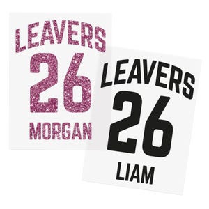 May include: Two white rectangular designs with the text "LEAVERS 26 MORGAN" in glittery pink and "LEAVERS 26 LIAM" in black. The designs resemble sports jerseys, suitable for school or team events.