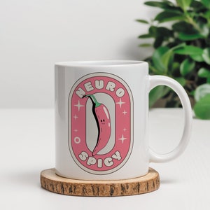 Puede incluir: Taza de cer&aacute;mica blanca con una pegatina rosa y blanca que presenta un chile rojo con una cara sonriente y el texto "Neuro Spicy".