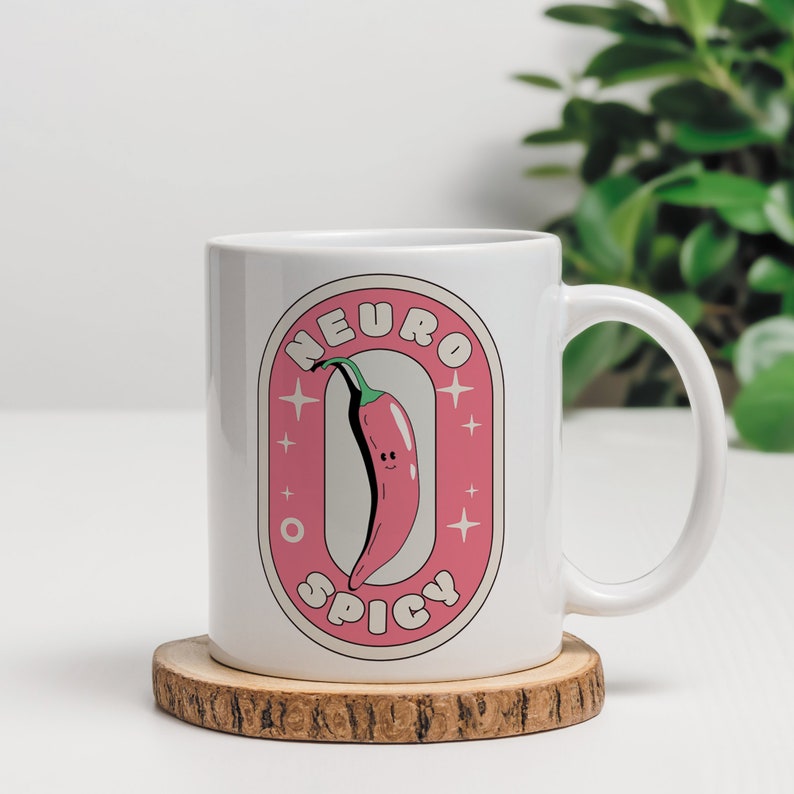 Puede incluir: Taza de cer&aacute;mica blanca con una pegatina rosa y blanca que presenta un chile rojo con una cara sonriente y el texto "Neuro Spicy".