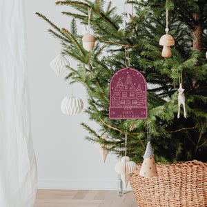 May include: Burgundy red wooden Christmas ornament with a white outline of a house and the text "Our First Christmas 20 24".