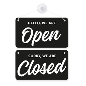 Op de afbeelding: Zwart rechthoekig bord met witte tekst. Boven staat "HELLO, WE ARE Open" in sierlijke letters, en daaronder "SORRY, WE ARE Closed". Ontworpen om openingstijden aan te geven.