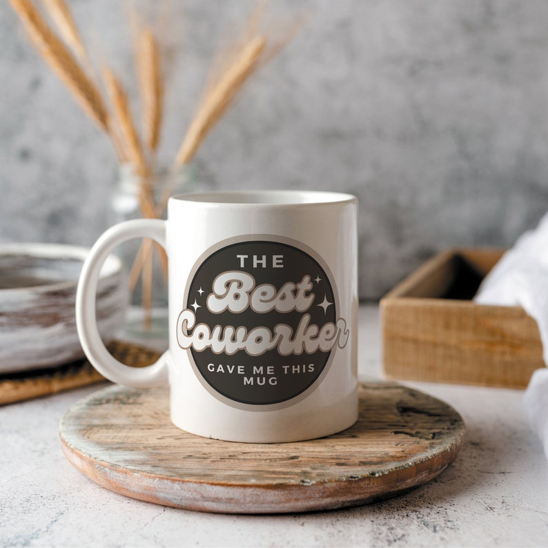 以下が含まれることがあります： 「The Best Coworker Gave Me This Mug」と書かれた黒い円形のデザインが施された白いセラミックマグカップです。