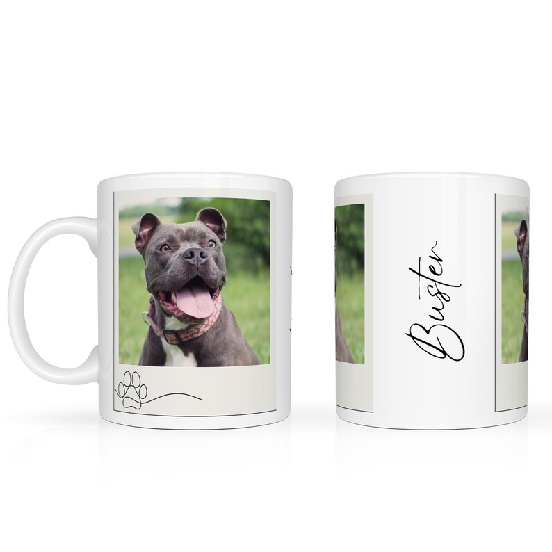May include: White ceramic mug featuring a photo of a gray dog with its tongue out, wearing a pink collar. The mug has the name "Buster" in cursive on the side and a paw print design.