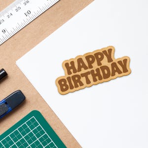May include: A brown paper card with the words "Happy Birthday" in a brown font.