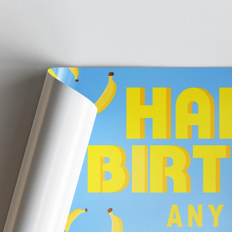May include: A blue poster with yellow text that reads "HAPPY BIRTHDAY ANY". The poster features yellow banana illustrations. The corner of the poster is peeled back, revealing a white surface.