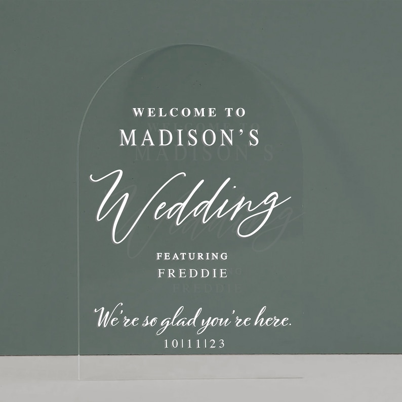 K&ouml;nnte beinhalten: Ein klares Acryl-Bogenschild mit dem Text "Willkommen zur Hochzeit von Madison mit Freddie" und "Wir freuen uns, dass Sie da sind." mit dem Datum 10.11.23.