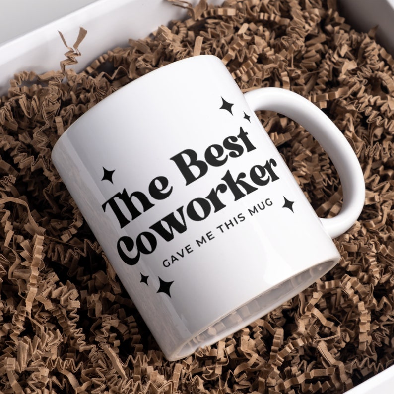 Op de afbeelding: Witte keramische mok met zwarte tekst die "The Best Coworker Gave Me This Mug" zegt met kleine sterretjesontwerpen.