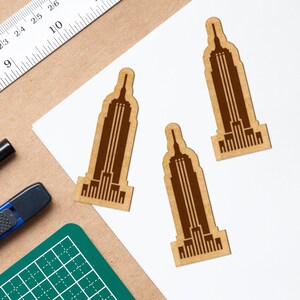 May include: Three brown paper cutouts of the Empire State Building on a white background. The cutouts are approximately 4 inches tall.